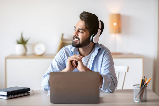 Mosolygó arab férfi fülhallgató zenét hallgat, miközben dolgozik a laptop - Fotó, kép