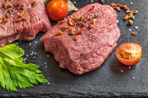 fresh raw meat with cherry tomatoes, spices and herbs on a black slate surface - Photo, Image