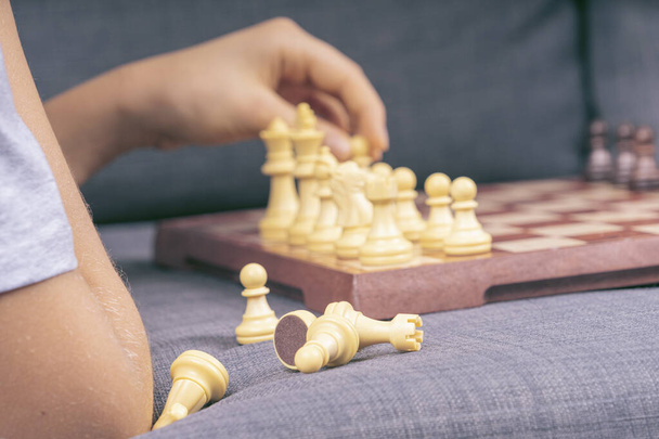 Closeup de meninos mão segurando figura de xadrez enquanto joga xadrez em casa. Educação, jogo de tabuleiro estratégico, lazer, entretenimento em casa - Foto, Imagem