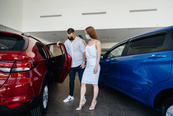 Young couple in masks selects a new vehicle and consult with a representative of the dealership in the period of the pandemic. Car sales, and life during the pandemic - Foto, imagen