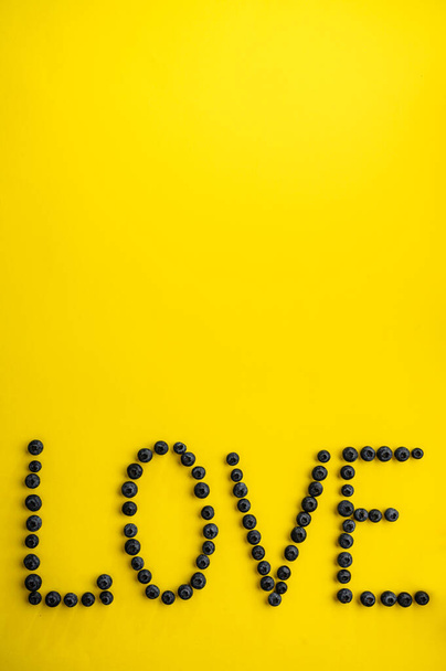 Blueberries love word on yellow background, top view. Organic vegetarian food, grocery assortment, natural eco products, healthy lifestyle concept - 写真・画像
