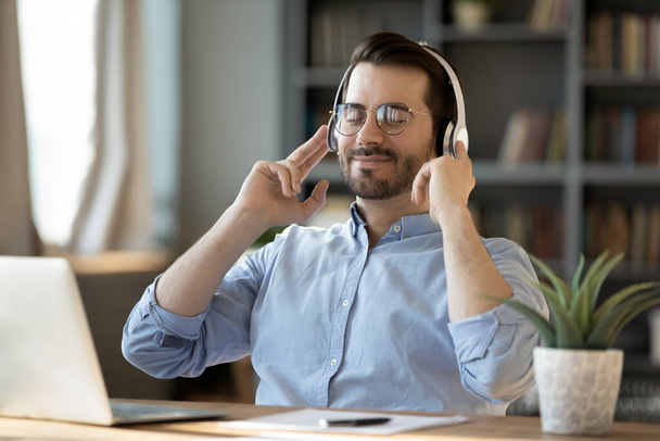 Relaxed young happy businessman listening music in headphones. - Фото, изображение