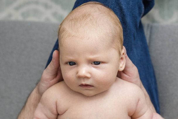 Πορτρέτο ενός νεογέννητου μωρού που βρίσκεται στα πόδια ενός γονέα στο σπίτι. Χαριτωμένο καυκάσιο γυμνό μωρό με ανοιχτά μάτια. Ενός μηνός. Μάτια. Στο πάνω μέρος. Τρόπος ζωής. Έννοια της γονικής μέριμνας, φροντίδα του μωρού. Οριζόντια. - Φωτογραφία, εικόνα