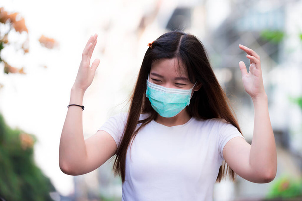 Beautiful young woman wearing green medical face mask for coronavirus disease (COVID-19) and pm2.5 dust. Get upset with harsh environments. A new outbreak concept. - Photo, Image