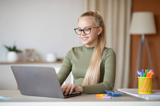 Χαρούμενη έφηβη που κάθεται στο σπίτι χρησιμοποιώντας το laptop - Φωτογραφία, εικόνα
