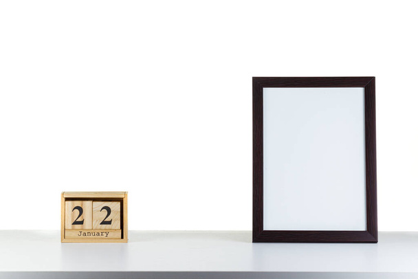 Ξύλινο ημερολόγιο 22 Ιανουαρίου με πλαίσιο για φωτογραφία σε λευκό τραπέζι και φόντο close-up - Φωτογραφία, εικόνα