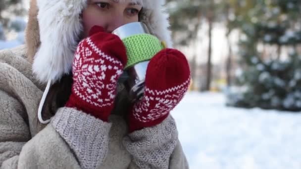 Mladá žena stojí v zimním lese nebo parku a pije horký čaj - Záběry, video