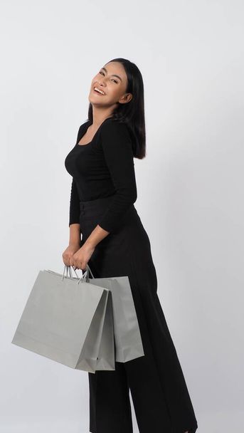 Shopping. Confident and sexy young Asian woman happily with shopping bag isolated on white studio background. Shopping woman in black dress happy smiling holding shopping bags. joyful playful active shopaholic girl.  - Fotografie, Obrázek