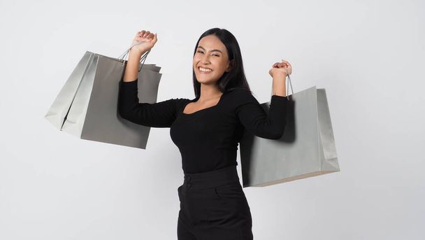 Ψώνια. Αυτοπεποίθηση και σέξι νεαρή ασιατική γυναίκα ευτυχώς με τσάντα ψώνια απομονώνονται σε λευκό φόντο στούντιο. Ψώνια γυναίκα με μαύρο φόρεμα χαρούμενη χαμογελώντας κρατώντας τσάντες για ψώνια. χαρούμενο παιχνιδιάρικο ενεργό shopaholic κορίτσι.  - Φωτογραφία, εικόνα