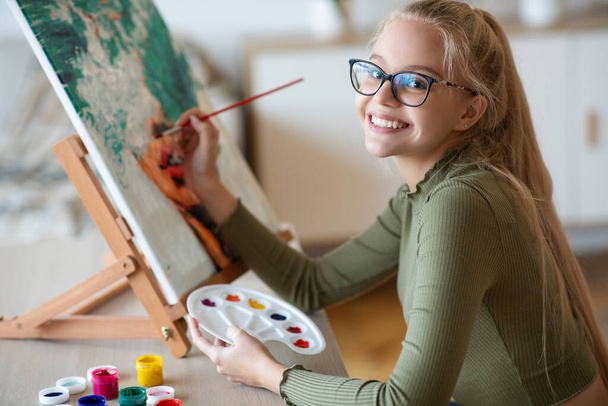 Inspirált tini lány festmény gazdaság ecset és paletta, festmény - Fotó, kép