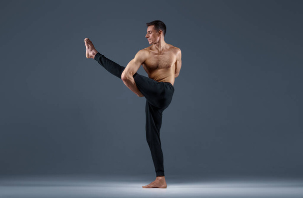 Männliches Yoga bei Stretching-Übungen im Studio, grauer Hintergrund. Starker Mann praktiziert Yogi, Asana-Training, höchste Konzentration, gesunder Lebensstil - Foto, Bild