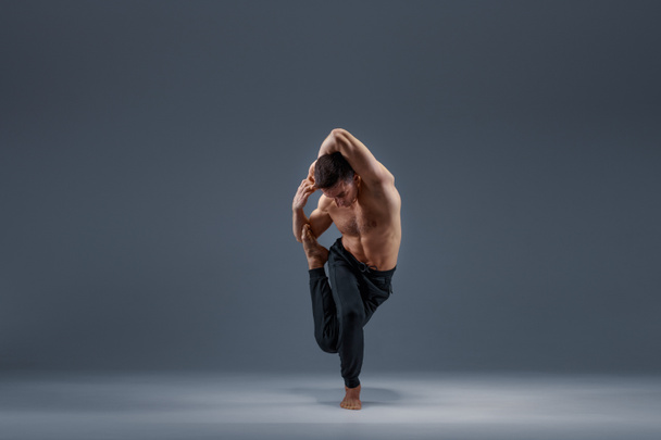 Yoga facendo esercizio di stretching in studio, sfondo grigio. Uomo forte che pratica yogi, allenamento asana, concentrazione massima, stile di vita sano - Foto, immagini