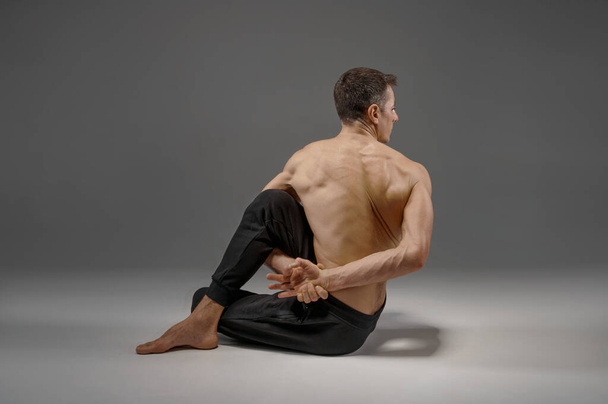 Yoga beim Stretching im Studio, grauer Hintergrund. Starker Mann praktiziert Yogi, Asana-Training, höchste Konzentration, gesunder Lebensstil - Foto, Bild