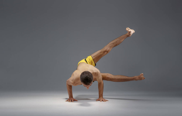 Yoga musculaire se tient sur les mains dans la pose difficile, position de méditation, fond gris. Homme fort faisant de l'exercice de yogi, l'entraînement d'asana, la concentration supérieure, mode de vie sain - Photo, image