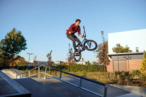 Мужчина байкер bmx, прыжок в действии, подросток на тренировке в скейтпарке. Велоспорт, опасные велосипедные упражнения, рискованная уличная езда, езда на велосипеде в летнем парке - Фото, изображение