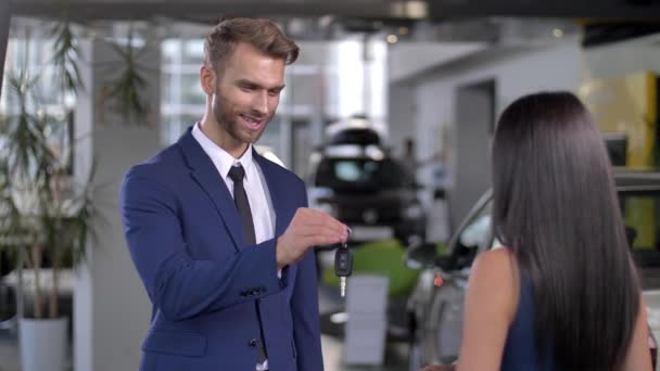 Auto distribuidor sonriente dando llave del coche a comprador femenino - Imágenes, Vídeo