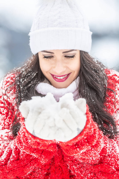 Egy piros pulóveres nő hóeséssel borítva mosolyog egy maroknyi hóra a kezében.. - Fotó, kép