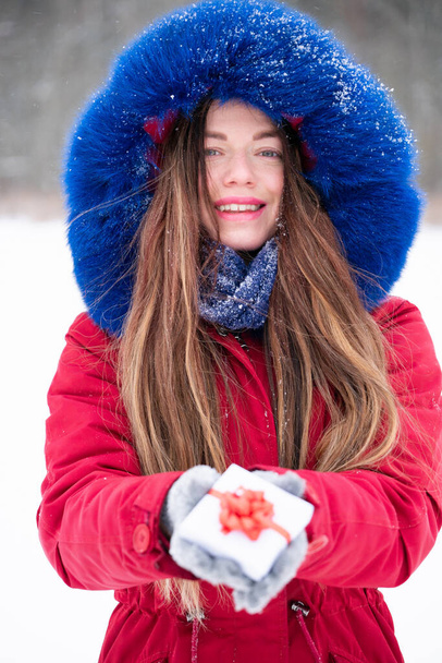 Young smiling woman in red hold gift box outdoors - Фото, изображение