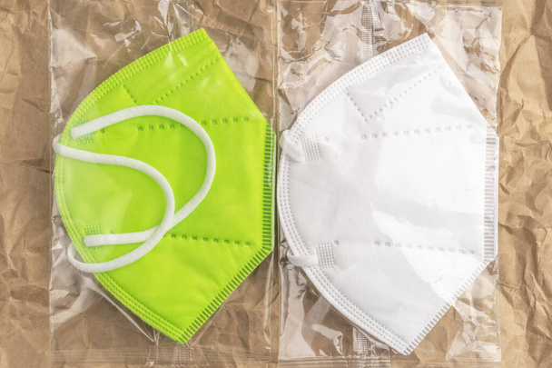 El respirador protector KN95 se enmascara en un embalaje de plástico brillante sobre un fondo de papel arrugado y arrugado. Verde y blanco. - Foto, imagen