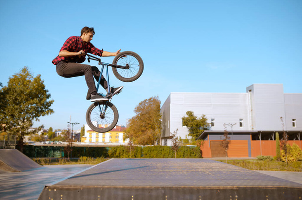 Man bmx biker springt op schans, tiener op training in skatepark. Extreme fiets sport, gevaarlijke fiets oefening, risico straat rijden, fietsen in de zomer park - Foto, afbeelding