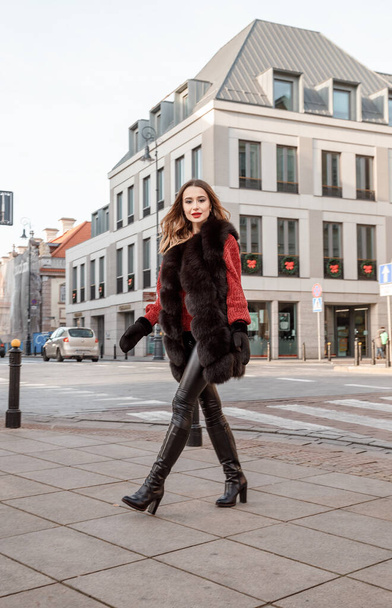 Outdoor photo of fashionable female model walking around city in winter vacation. Fashionable girl walking on Warsaw street in Old Town. - Фото, изображение