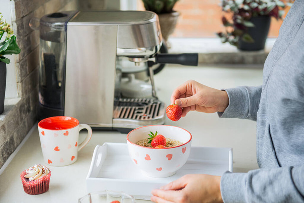 Woman adding strawberry fruits to oatmeal porridge bowl. Preparing surprise breakfast for lover on Valentines day. Simple festive healthy food idea. Copy space. Selective focus. - Fotografie, Obrázek