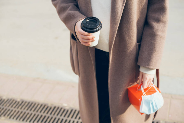 Donna in cappotto invernale sta bevendo portare via una tazza di caffè per strada durante le restrizioni pandemiche covid, bella giornata di sole. Focus selettivo. - Foto, immagini