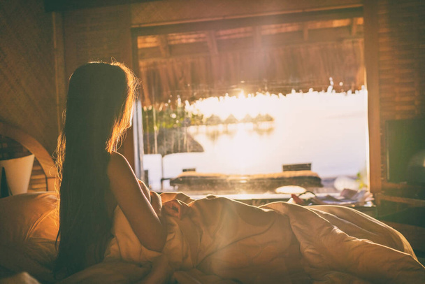 Luxus-Hotelzimmer Flitterwochen-Urlaub im Luxus-Resort - Mädchen wacht im Bett auf und blickt auf Meerblick in Overwater-Bungalow in Bora Bora, Tahiti, Französisch-Polynesien - Foto, Bild