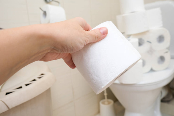 Wiele rolki papieru toaletowego w domu zbieracza, kupując zbyt wiele środków higienicznych podczas pandemii, ręka trzymając rolkę papieru toaletowego w łazience - Zdjęcie, obraz