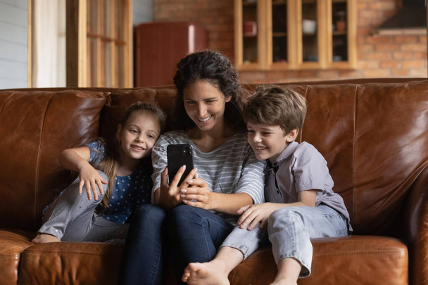 Happy mom and small kids watch video on cellphone - Valokuva, kuva