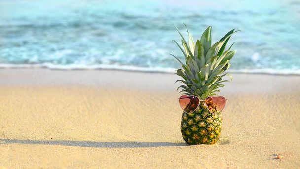 Ananas de mode avec des lunettes en forme de coeur sur une plage de sable - Photo, image