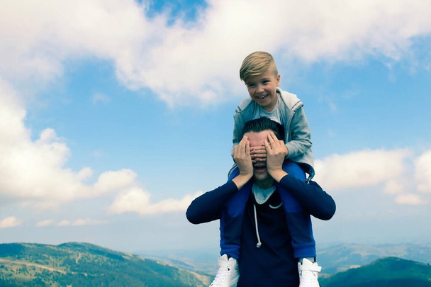 Zorgeloze vader en zoon die plezier hebben terwijl ze een dag in de bergen tegen de hemel doorbrengen.  - Foto, afbeelding