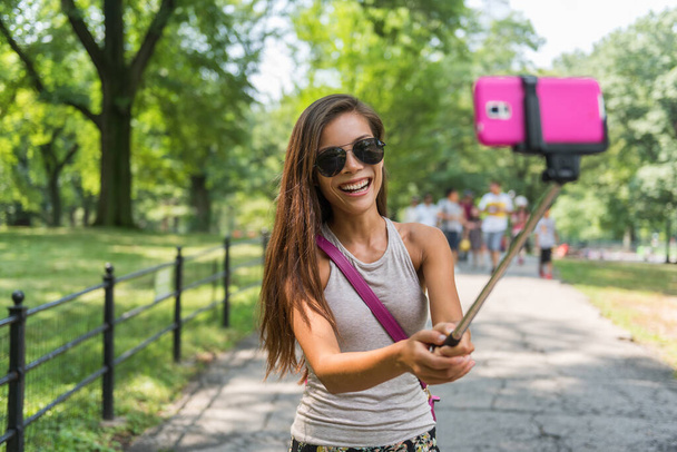 New York City tourist taking selfie stick photo in Central park, NYC. Happy travel Asian girl self-portrait picture with mobile phone at popular attraction walking in summer park in Manhattan, USA - Valokuva, kuva