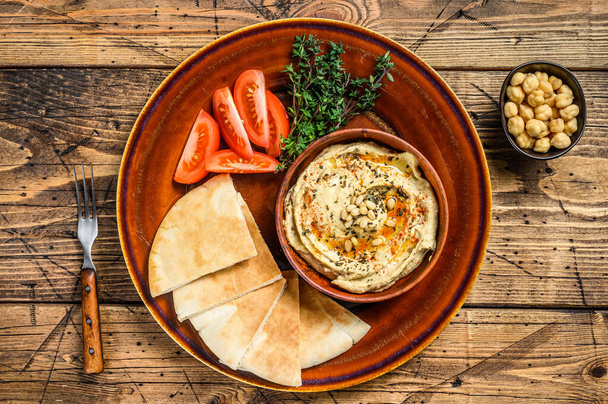 Hummus fresco con pan de pita, tomate y perejil en un plato rústico. fondo de madera. Vista superior. - Foto, imagen