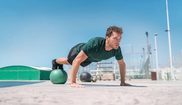 Fit exercises man strength training core doing balance push-ups workout at outdoor gym balancing on stability medicine ball with legs. Bodyweight pushups exercises. Push-up variation - Foto, Imagem
