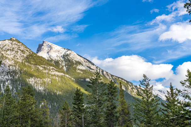 Snow-covered Mount Rundle mountain range with snowy forest over blue sky and white clouds in winter sunny day. Banff National Park, Canadian Rockies. - Photo, Image