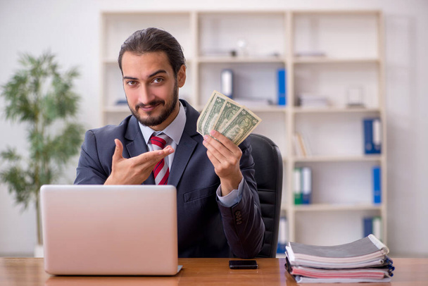 Молодой работник мужского пола держит банкноты в офисе - Фото, изображение