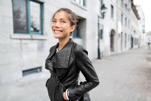 CIty lifestyle people - Young happy Asian woman walking on Europe old port street smiling wearing black leather jacket outside. Urban cool stylish chinese caucasian girl in autumn fall winter - Photo, image