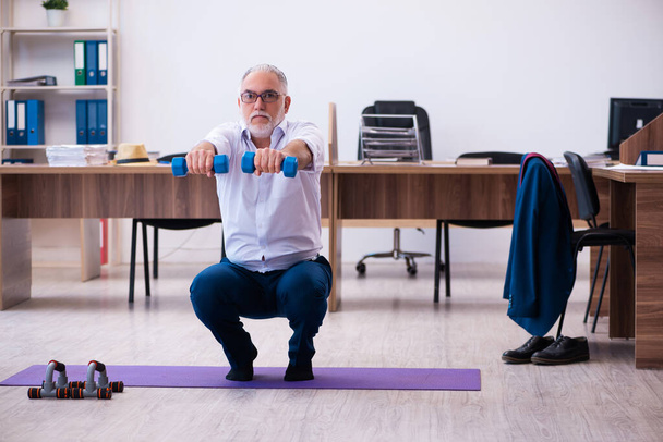 Vieil homme d'affaires employé faisant des exercices sportifs dans le bureau - Photo, image