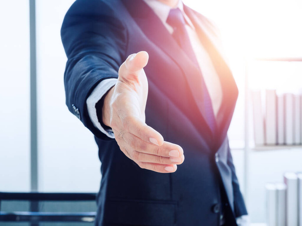 A Businessman with open hand ready for seal a deal on modern office background with success light. Business man in suit hold out one's hand waiting for shaking hands. Partner handshake. Focus on hand. - Photo, Image