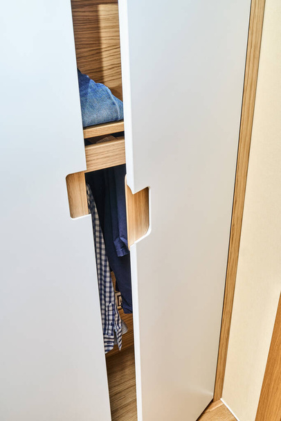 Detail of the wardrobe close-up. Opened wooden wardrobe with flat finger pull wardrobe doors. Oak veneered plywood cabinets with light gray painted cabinet doors. Modern furniture - Foto, afbeelding