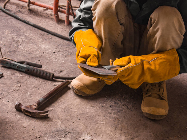 A man inspects a makeshift scraper or putty knife created onsite with leftover metal parts at a construction site. - Photo, Image