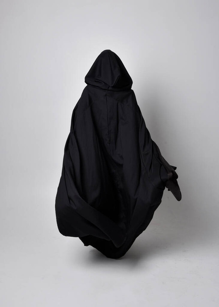 Ganztägiges Porträt einer hübschen schwarzhaarigen Frau, die einen langen dunklen Nada-Mantel trägt. Stehende Pose mit dem Gesicht zur Kamera, vor Studiohintergrund. - Foto, Bild