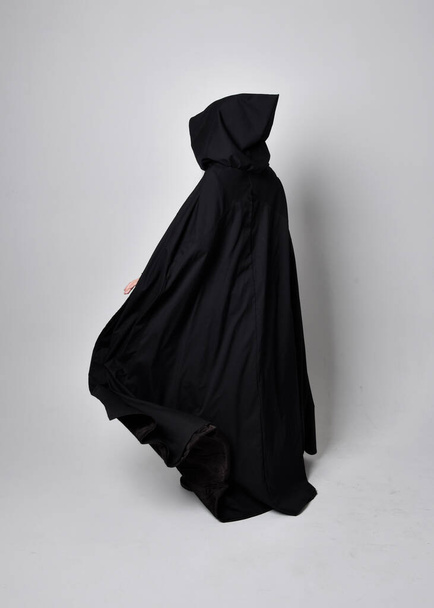 Retrato de comprimento total de mulher de cabelos pretos bonita vestindo manto longo vestido escuro nada. Posição em pé de frente para longe da câmera, contra um fundo de estúdio. - Foto, Imagem