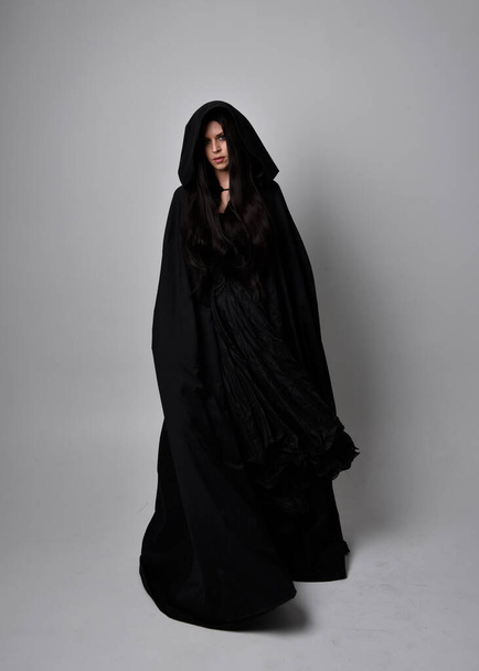 Portrait pleine longueur de jolie femme aux cheveux noirs portant une longue robe noire manteau nada. pose debout face à la caméra, sur fond de studio. - Photo, image