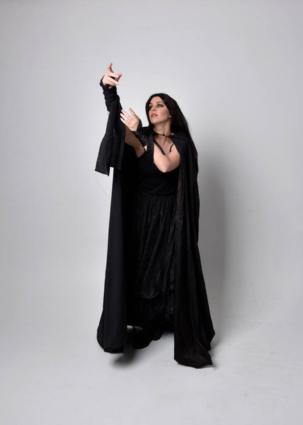 Portret pięknej czarnowłosej kobiety noszącej długi ciemny płaszcz nada. Stanąć twarzą do kamery, na tle studia. - Zdjęcie, obraz