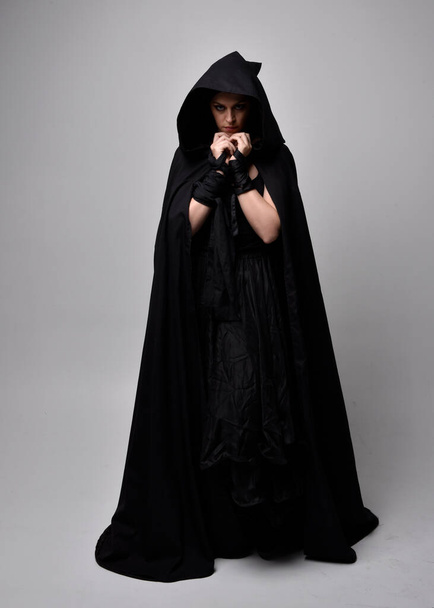 Портрет красивої чорної волохатої жінки в довгій темній сукні плаття плащ. Стоячи позаду камери, на фоні студії
. - Фото, зображення