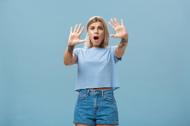 Woman terrified screaming and asking stop. Portrait of shocked panicking troubled blonde female in denim shorts and casual t-shirt pulling hands in no gesture dropping jaw and frowning - Photo, Image