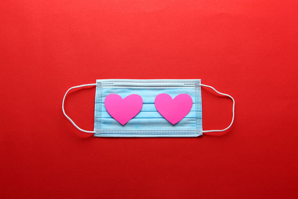 Dreilagige Schutzmaske für den klinischen Einsatz mit rosa Herzen auf rotem Hintergrund - Foto, Bild