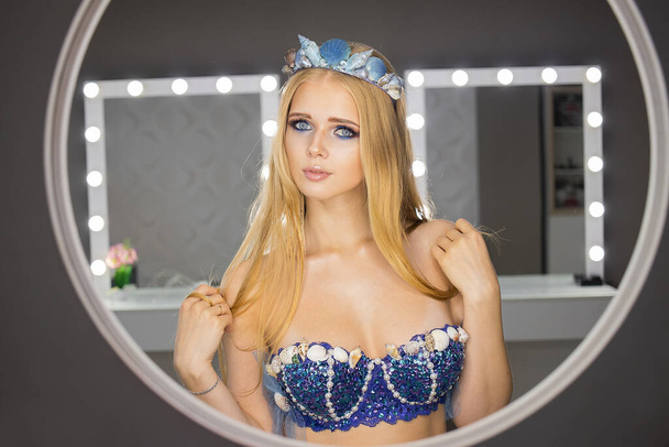 Jeune femme aux longs cheveux blonds debout devant le miroir regardant la caméra sur fond de miroirs - Photo, image